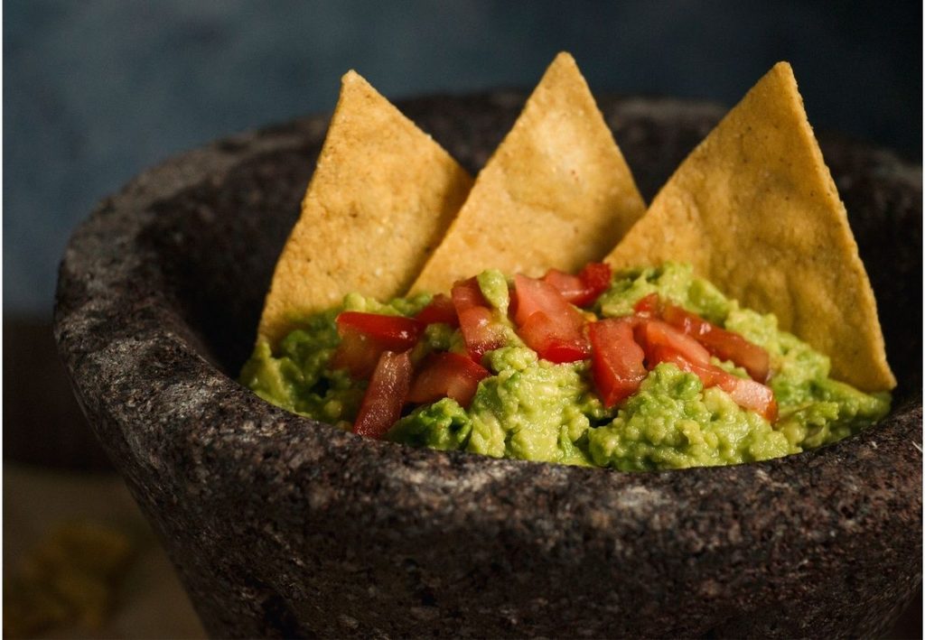 En mortel med guacamole toppad med tomat och natchochips.