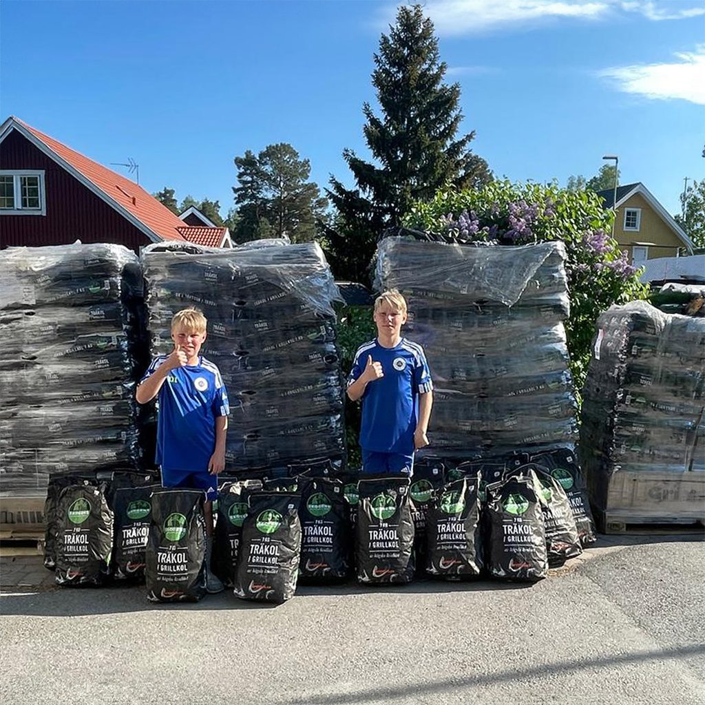 två pojkar står framför 4 pallar med grillkol.