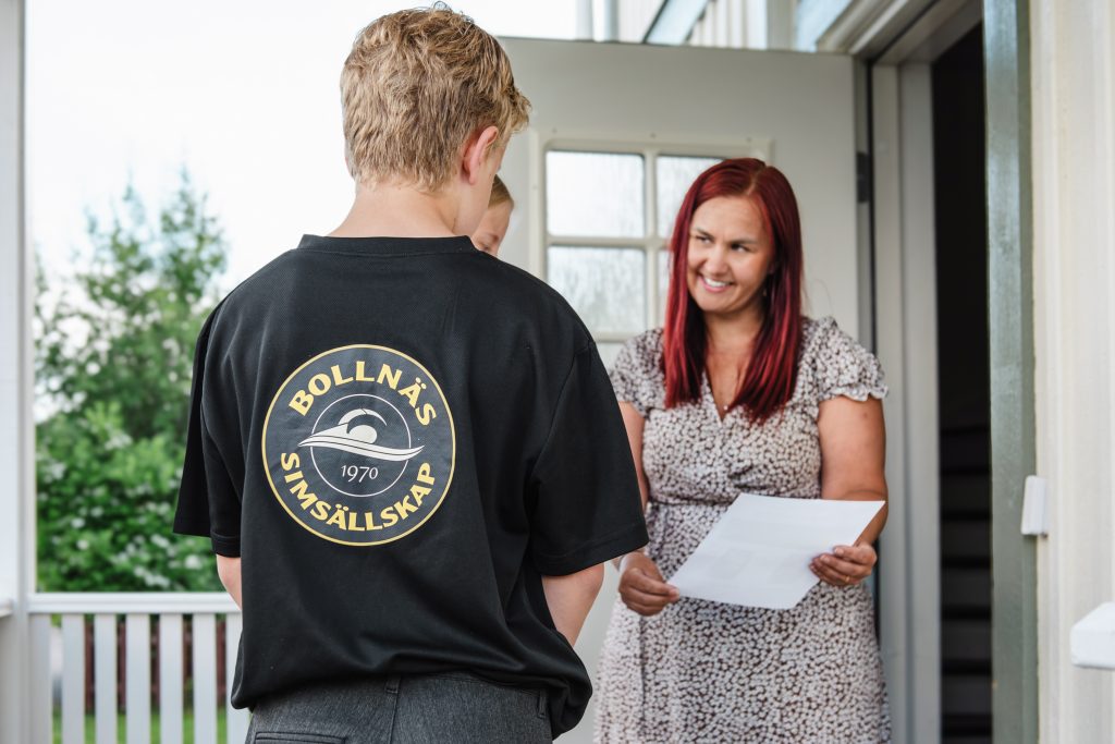 En ung kille sår framför en kvinna för att sälja kol. Kvinnan står i dörren med ett papper i handen.